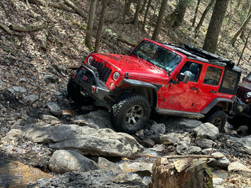 Red Jeep Wrangler navigating a rocky off-road trail equipped with an aftermarket steel bumper, winch, and lifted suspension.
