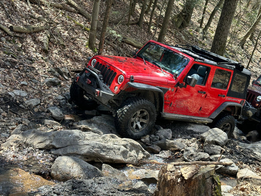 Red Jeep Wrangler navigating a rocky off-road trail equipped with an aftermarket steel bumper, winch, and lifted suspension.