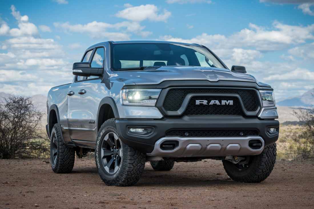 Silver Ram 1500 pickup truck with leveling kit and aggressive all-terrain tires on an off-road trail
