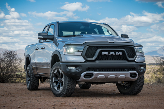 Silver Ram 1500 pickup truck with leveling kit and aggressive all-terrain tires on an off-road trail
