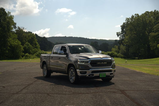 Modern RAM 1500 crew cab pickup truck featuring chrome front grille parked outdoors on a paved road in a scenic rural environment.
